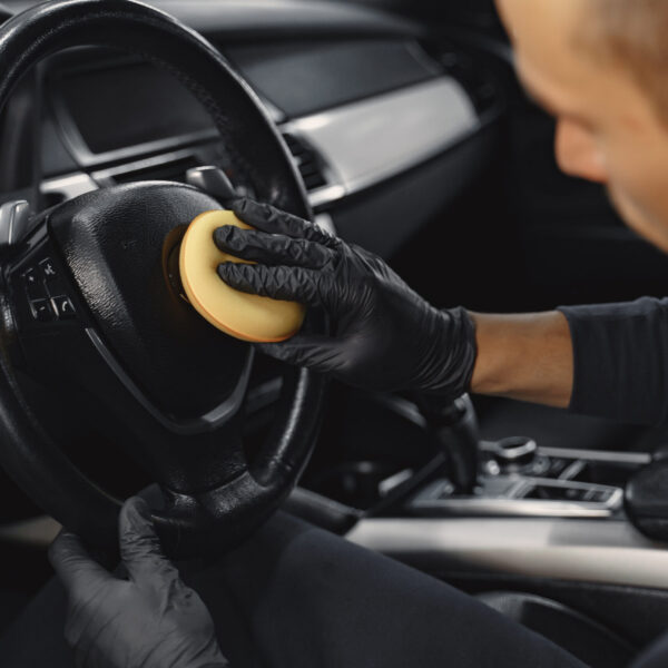 Man in a garage. Worker polish inside a car. Man in a black uniform.